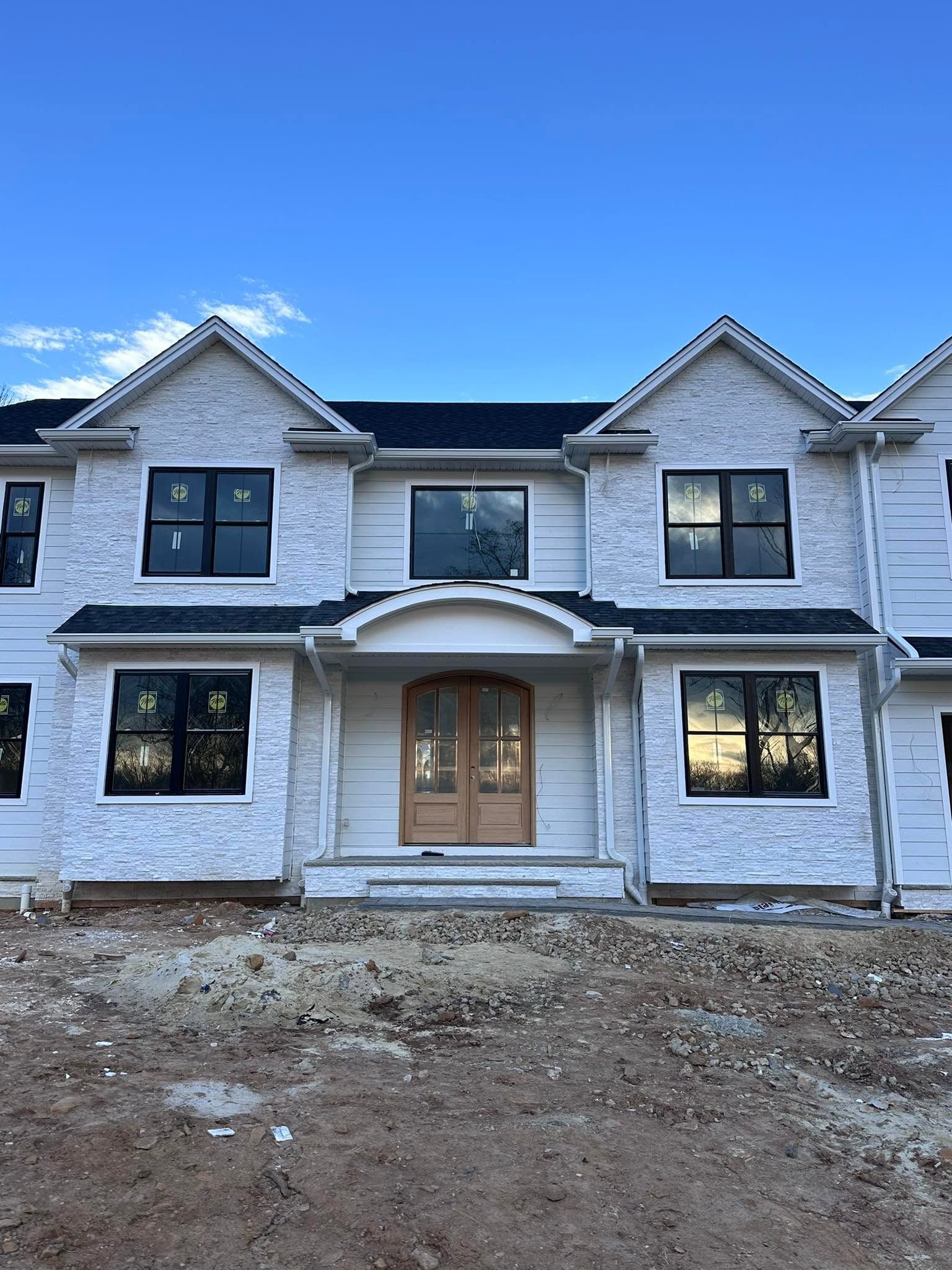 Newly built white stone two-story house with black windows and unfinished front yard at dusk