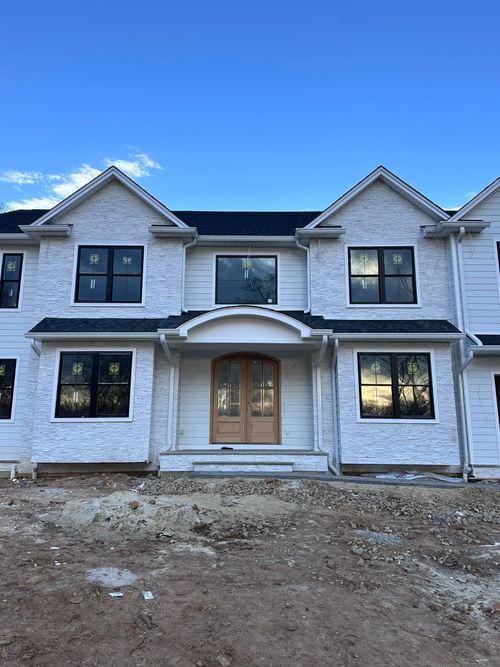 New two-story white house with black roof and large front windows under a blue sky