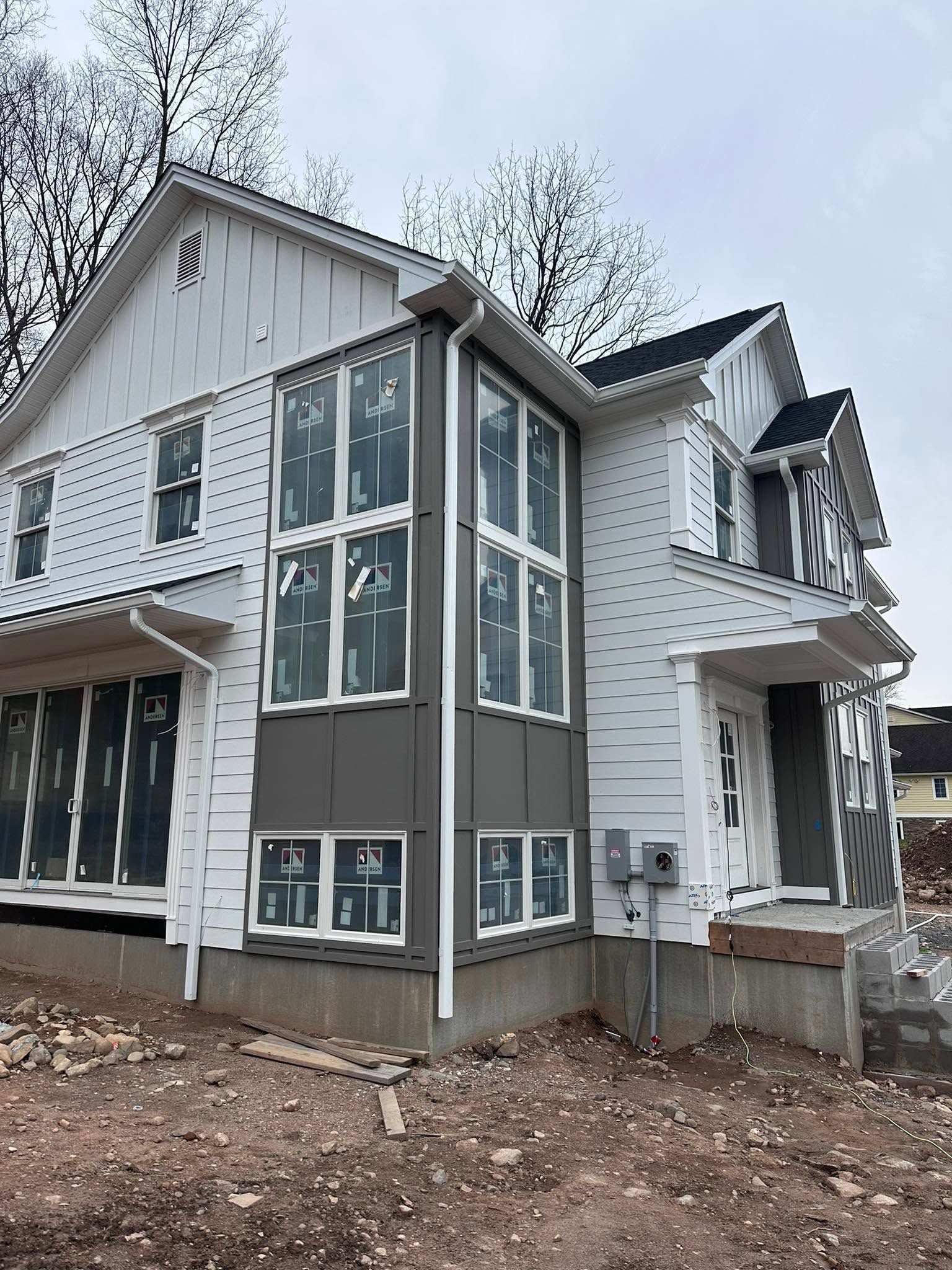 Partially built white and gray house with large windows on a bare dirt lot