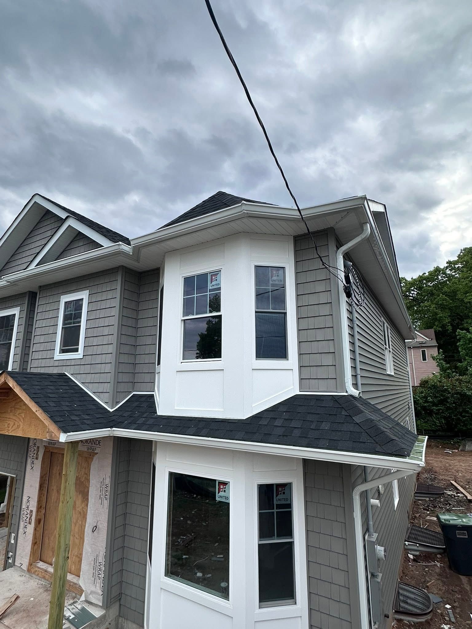 Two-story gray house with white trim and bay windows under construction or renovation