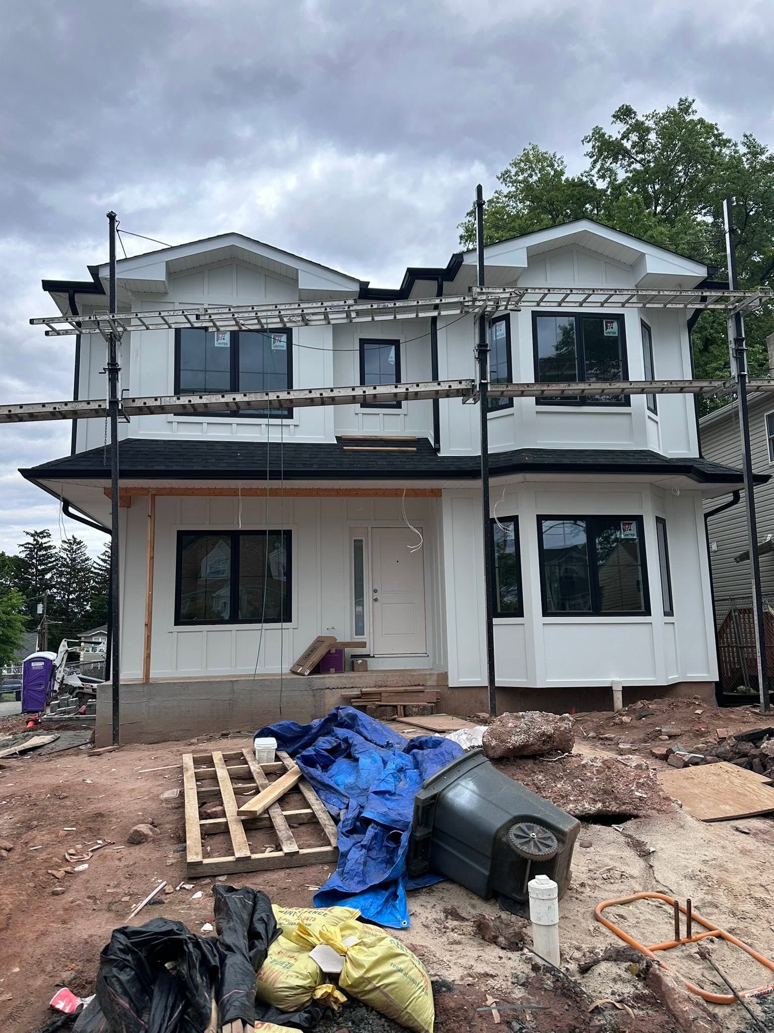 Two-story house under construction with scaffolding, unfinished walls, and debris in front
