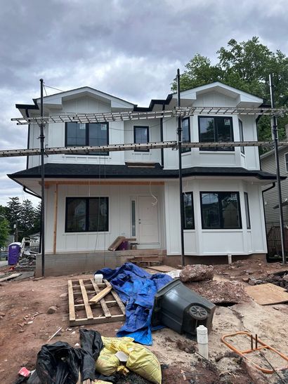 Two-story house under construction with scaffolding, unfinished walls, and debris in front