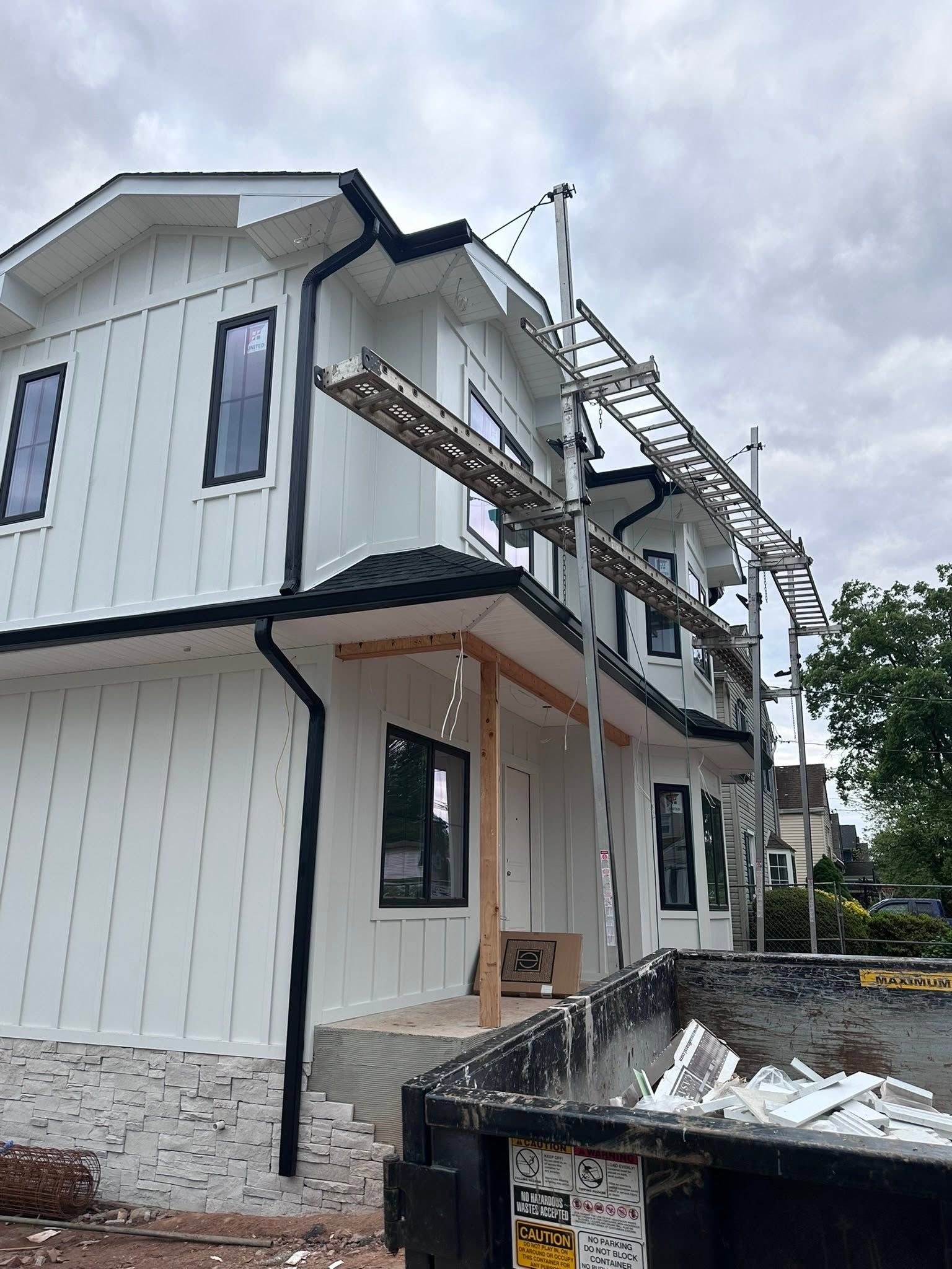 Two-story white house under construction with scaffolding, black trim, and gravel around the foundation.