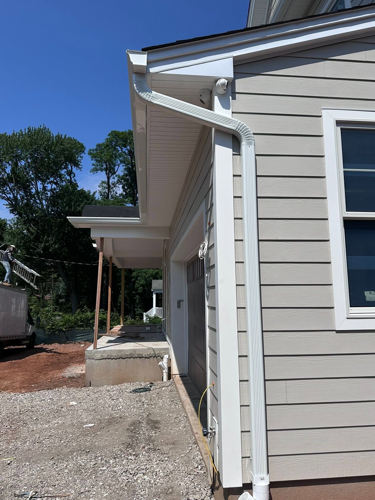 Side view of a gray house with white trim, gravel path, and a covered porch under a blue sky.