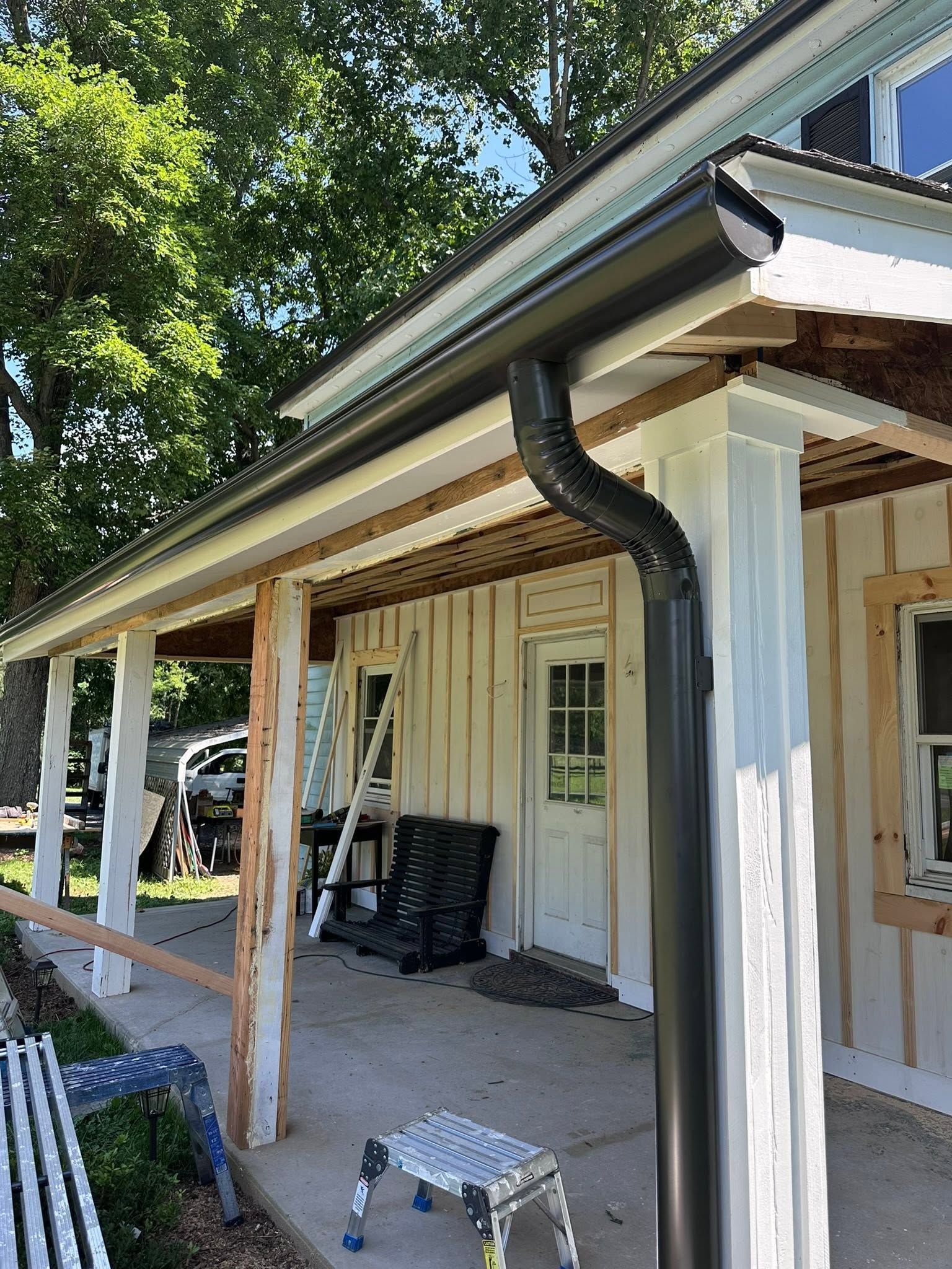 Covered porch with white columns, black gutter, and a ladder leaning against the house.