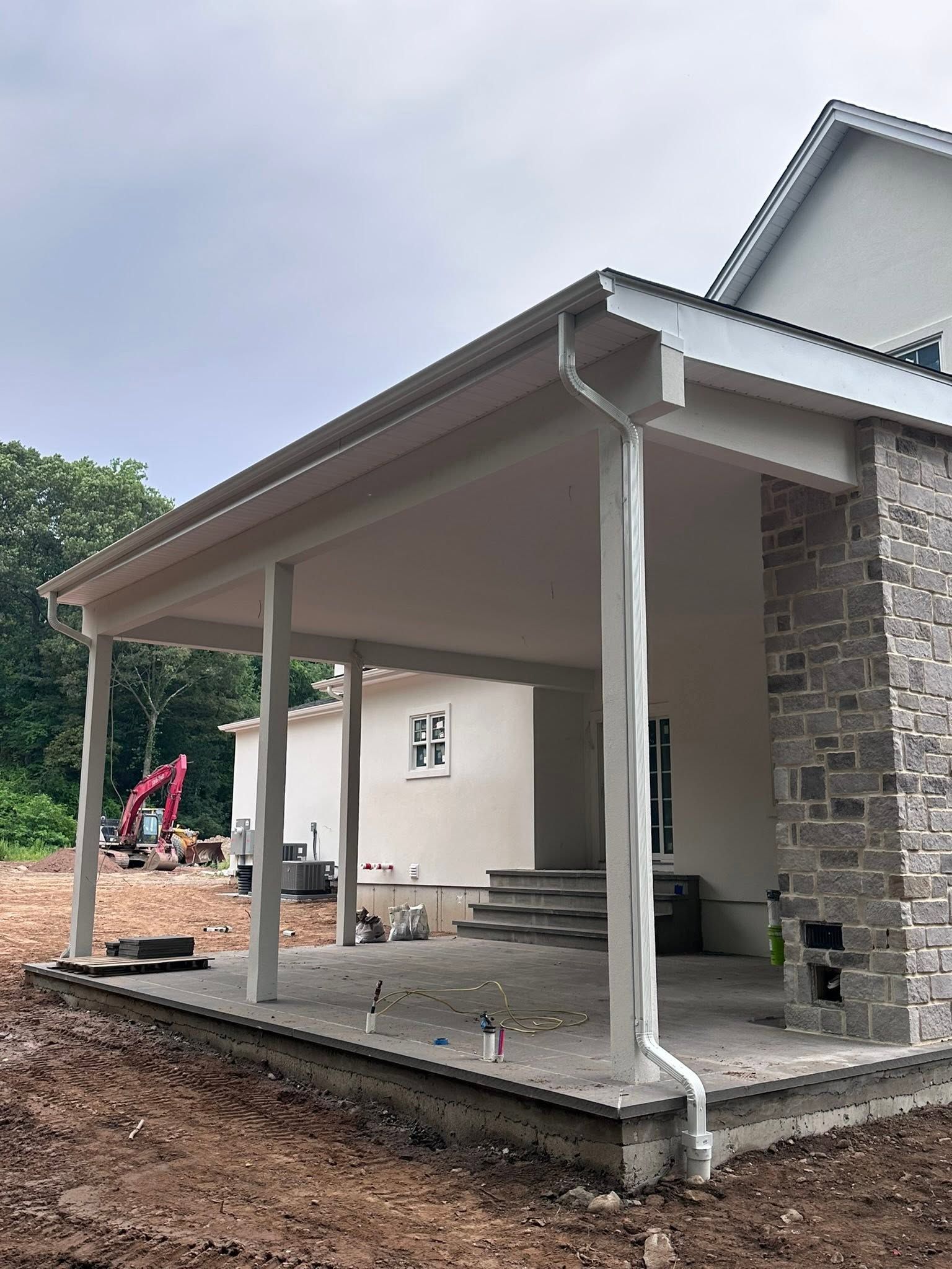 Partially built house with a covered porch, stone wall, and workers in the background