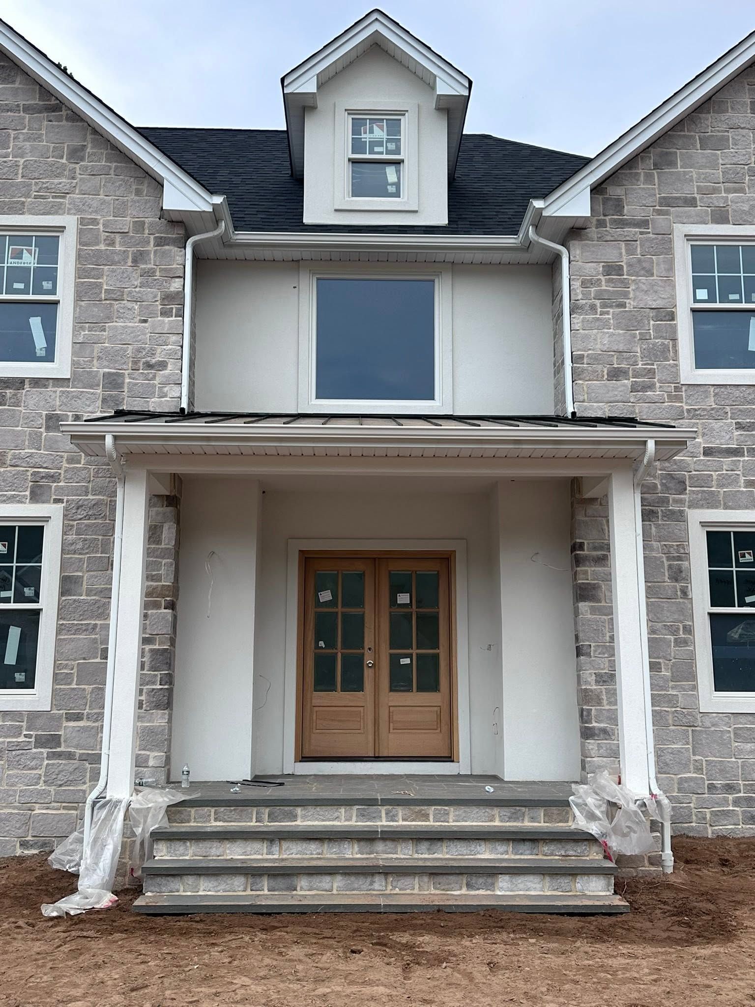 Front view of a gray stone house with wooden double doors and a small dormer above the porch