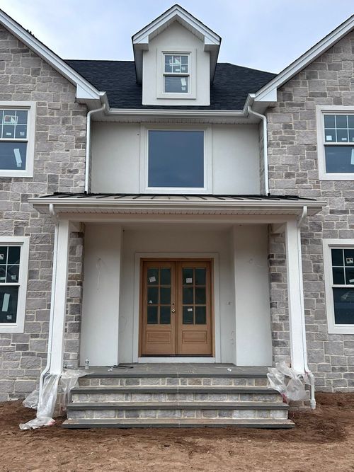 Front view of a gray stone house with wooden double doors and a small covered porch under construction.