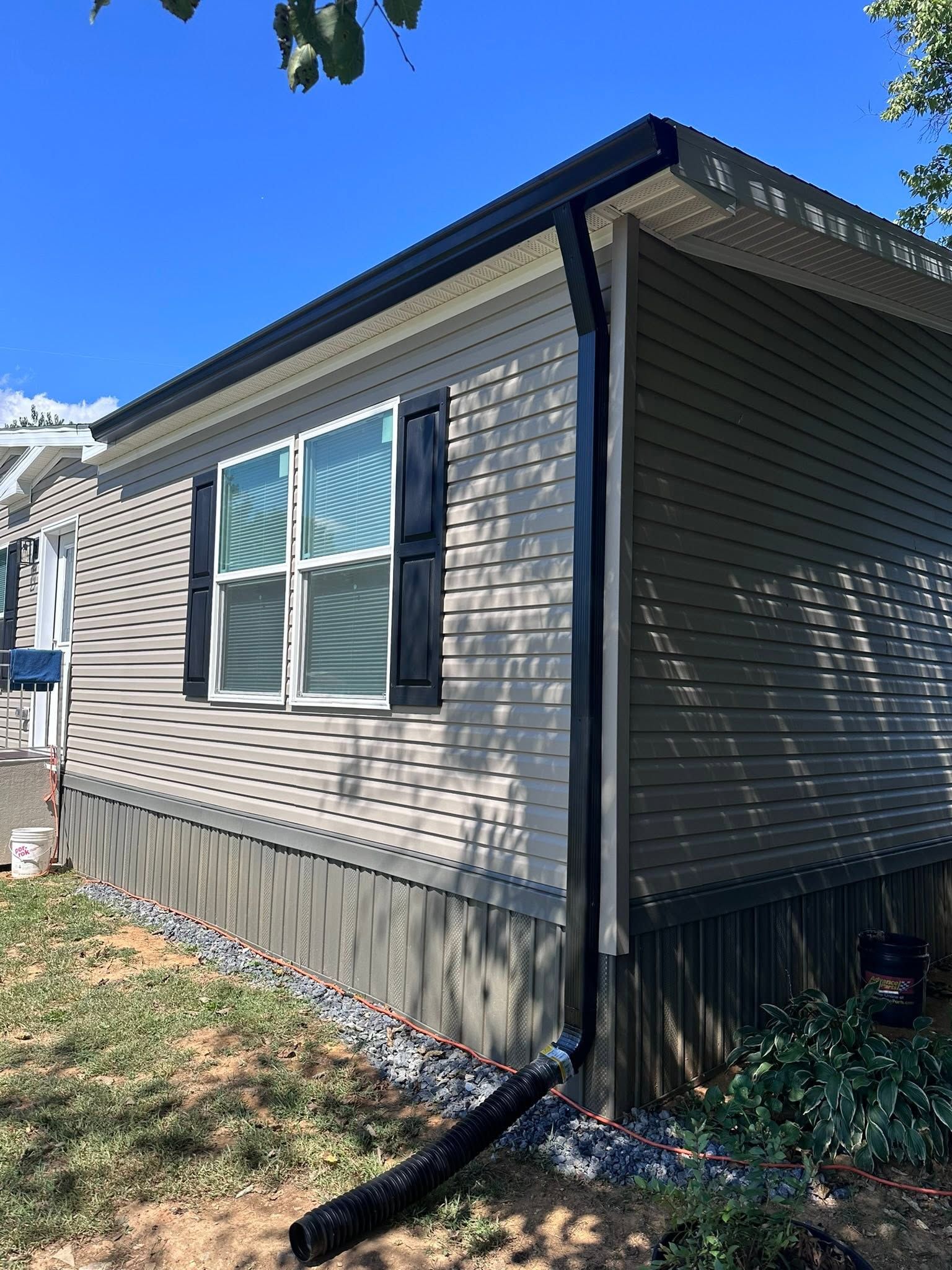 Side of a gray house with white-trimmed windows and a blue sky overhead.
