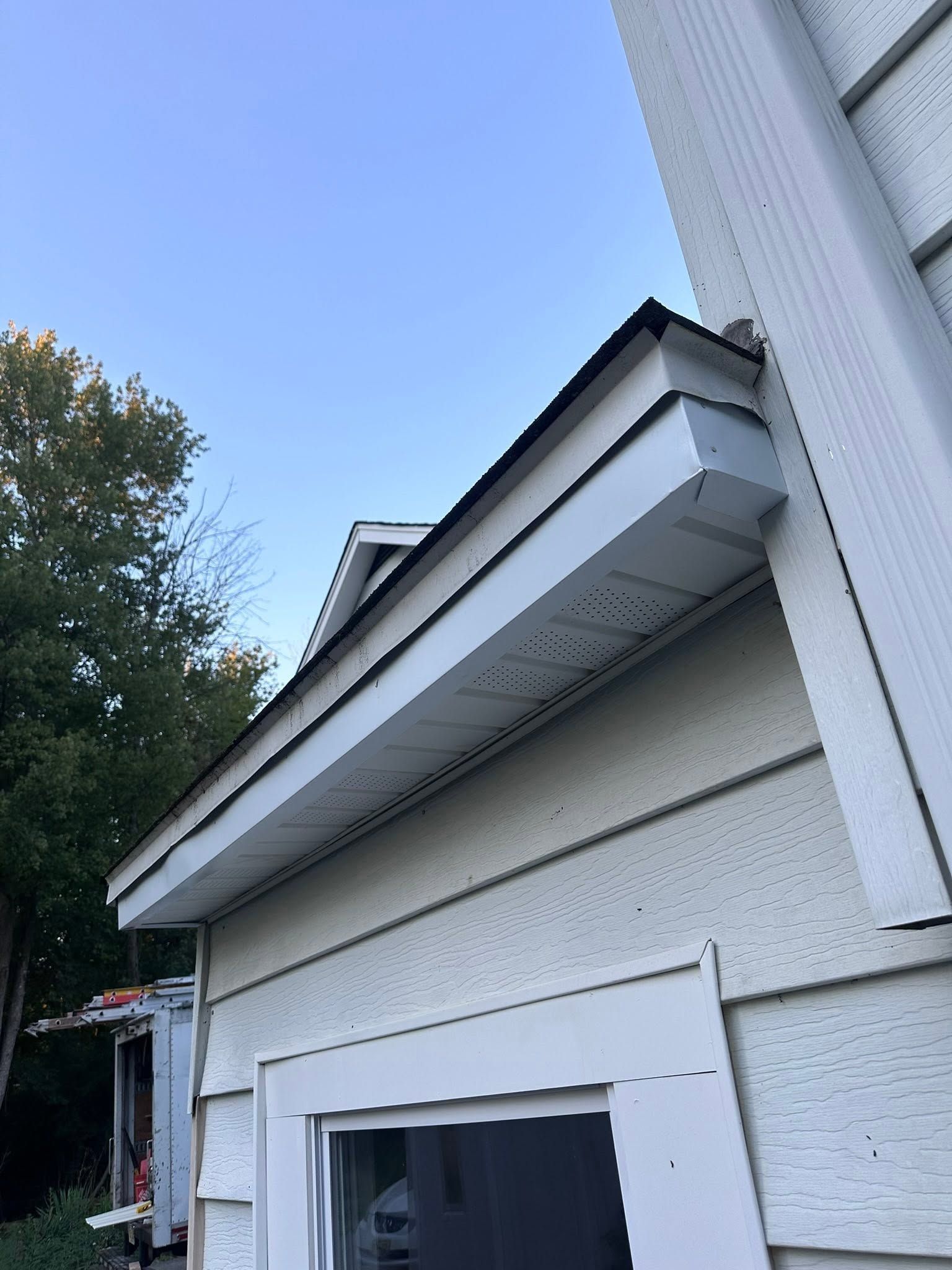 White house eaves and roofline beside a doorway, viewed from below against a blue sky.