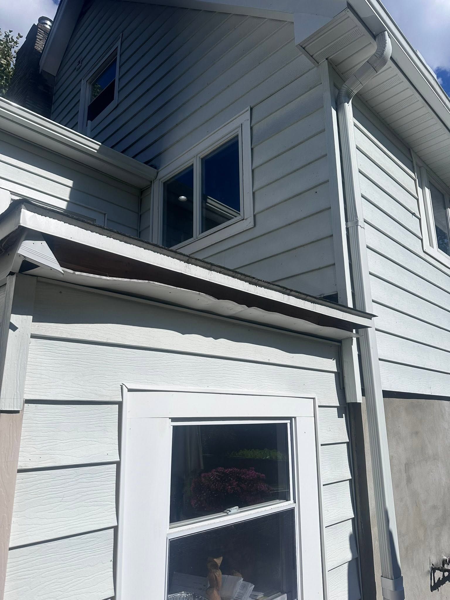 Gray house exterior with a small dormer and attached white-sided shed with a window