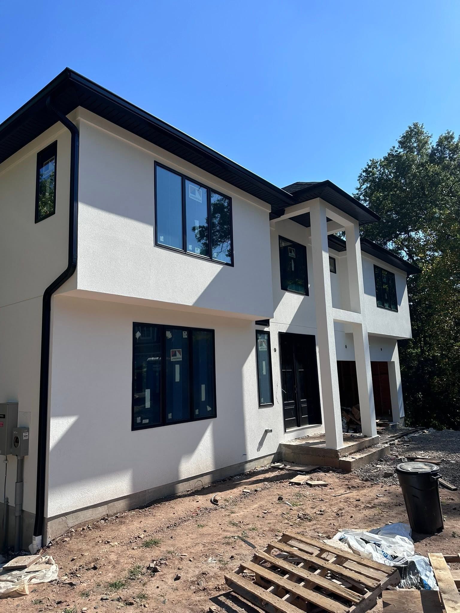 Two-story white house with black trim, blue windows, and a dirt front yard under construction