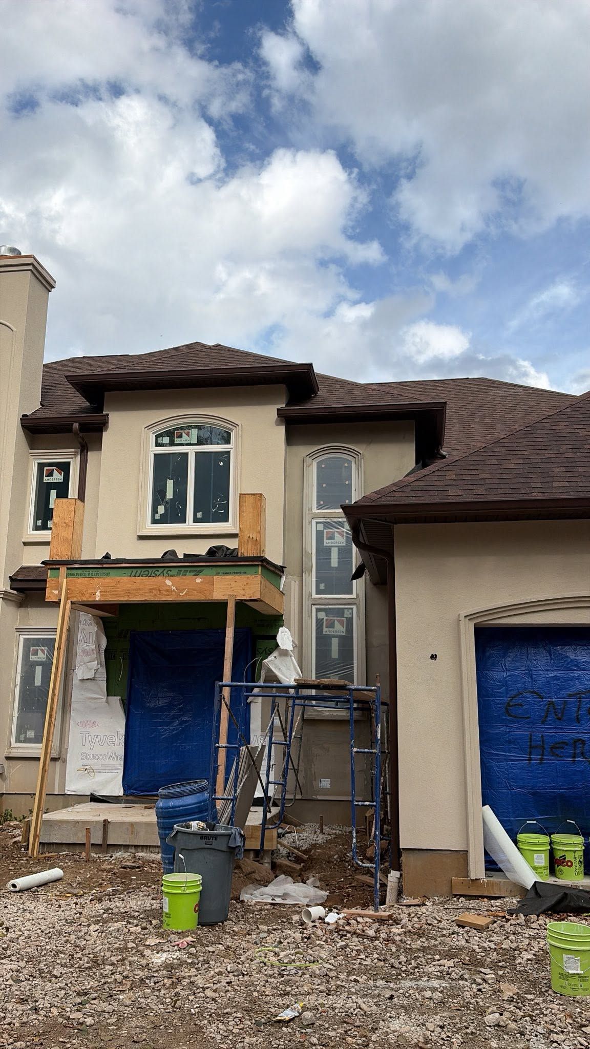 Partially renovated house with blue tarp-covered openings and debris in front under a cloudy sky