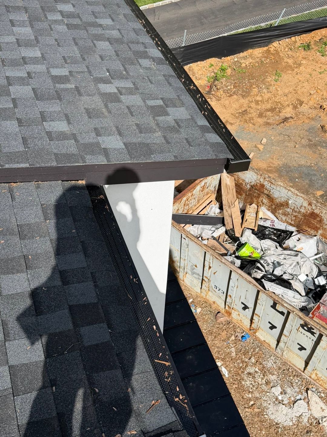 Roof shingles and gutter edge beside a construction debris pile below