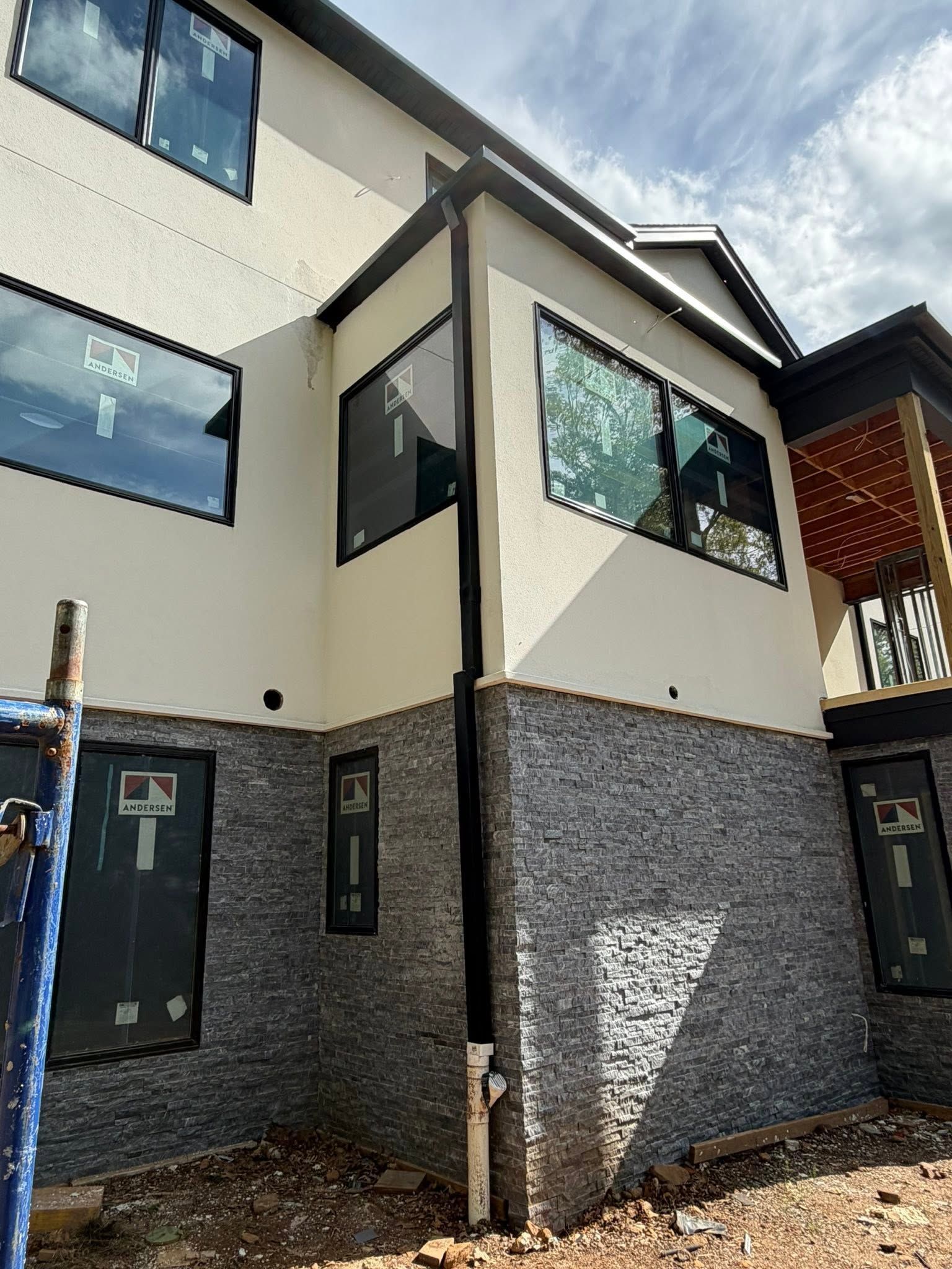 Modern townhouse exterior with cream walls, dark gray stone base, and large windows