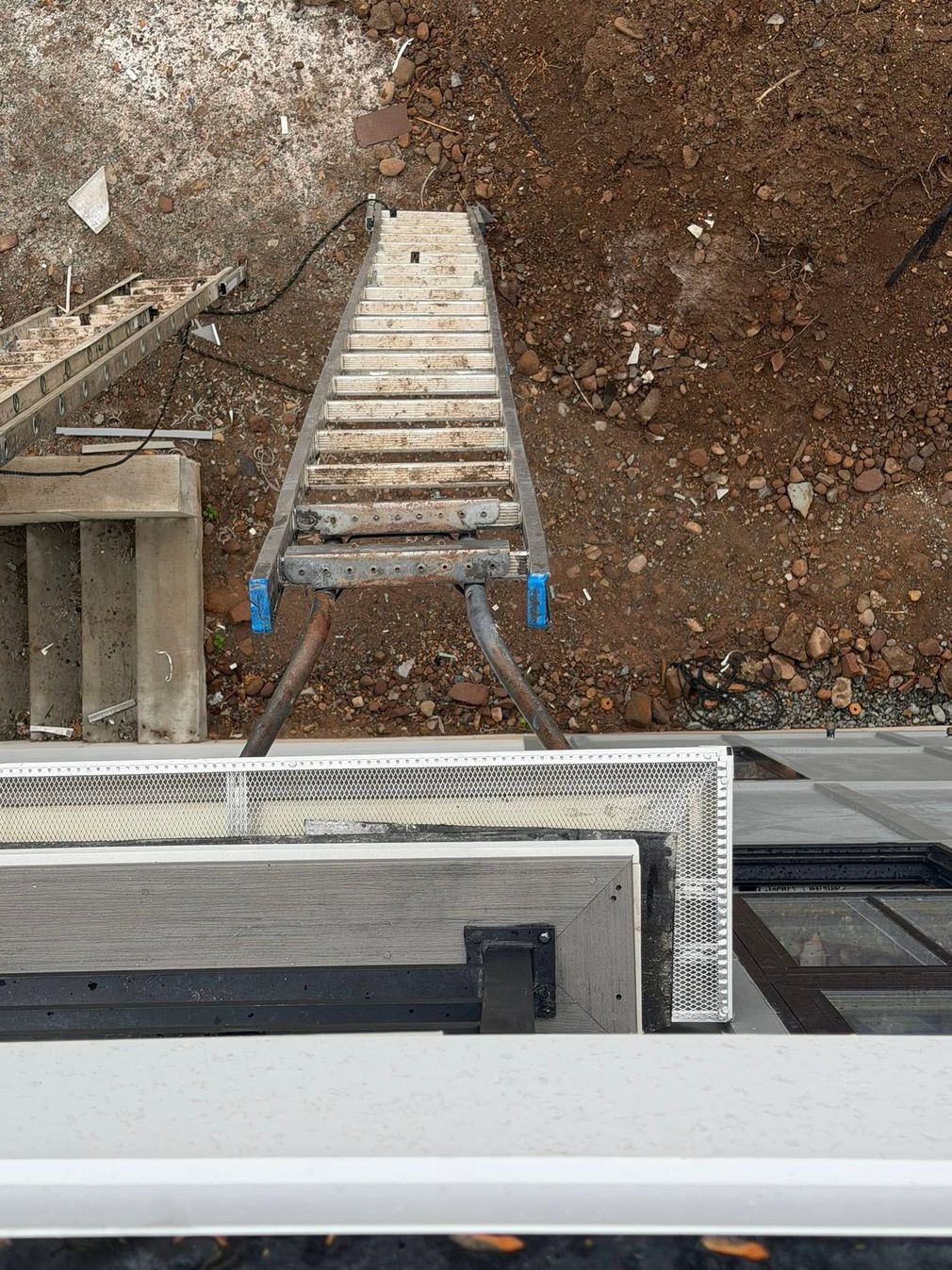 Top-down view of a dirt excavation with a wooden stairway and a building edge below