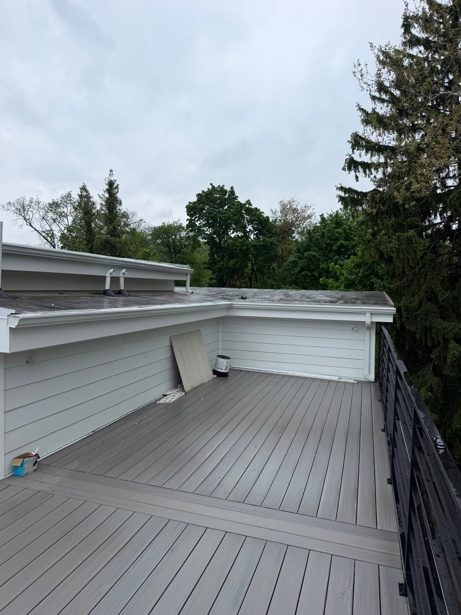 Roof deck with gray composite flooring, white railings, and trees under a cloudy sky