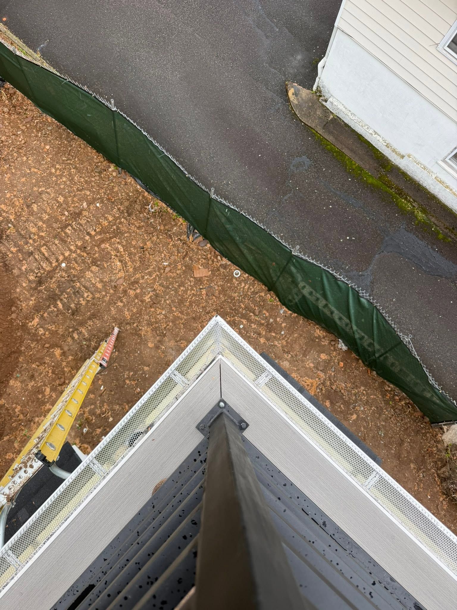 Aerial view of a building roof corner beside a paved path, green fence, and gravel ground