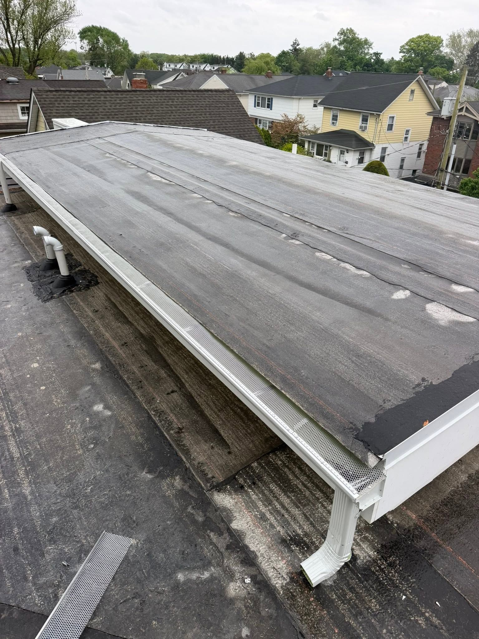 Roofing membrane on a flat rooftop with nearby houses and trees in the background