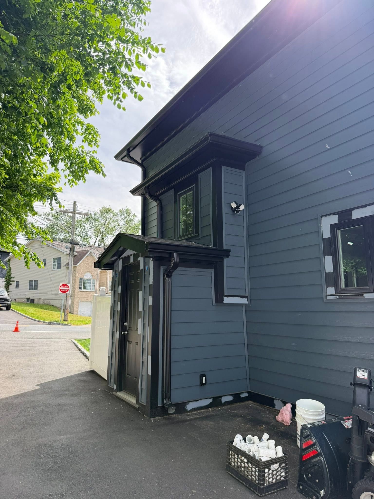 Dark blue building exterior with a small overhang, sidewalk, trees, and a parked scooter beside a wall