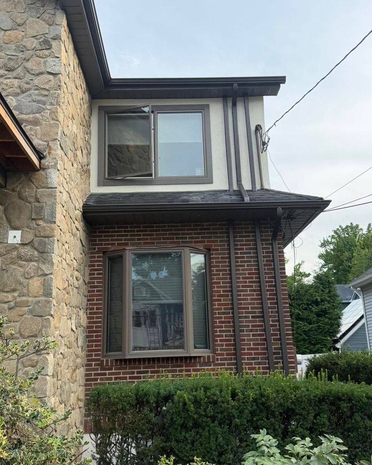 Two-story brick and stone house with bay windows and a hedge in front
