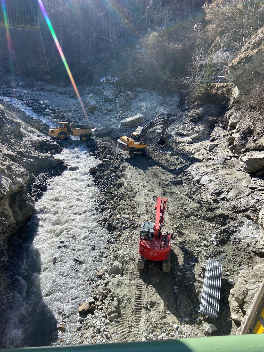 Une excavatrice rouge roule sur un chemin de terre à côté d'une rivière.