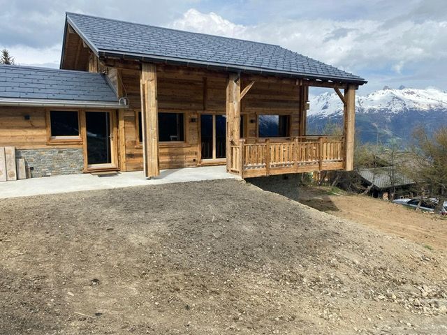 Une maison en bois avec un toit en ardoise est assise au sommet d'une colline de terre.