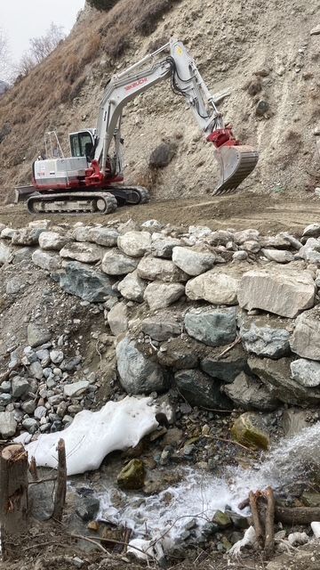 Une grande excavatrice travaille sur un mur rocheux à côté d'un ruisseau.
