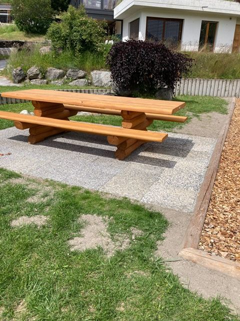 Une table de pique-nique en bois est posée dans l'herbe devant une maison.