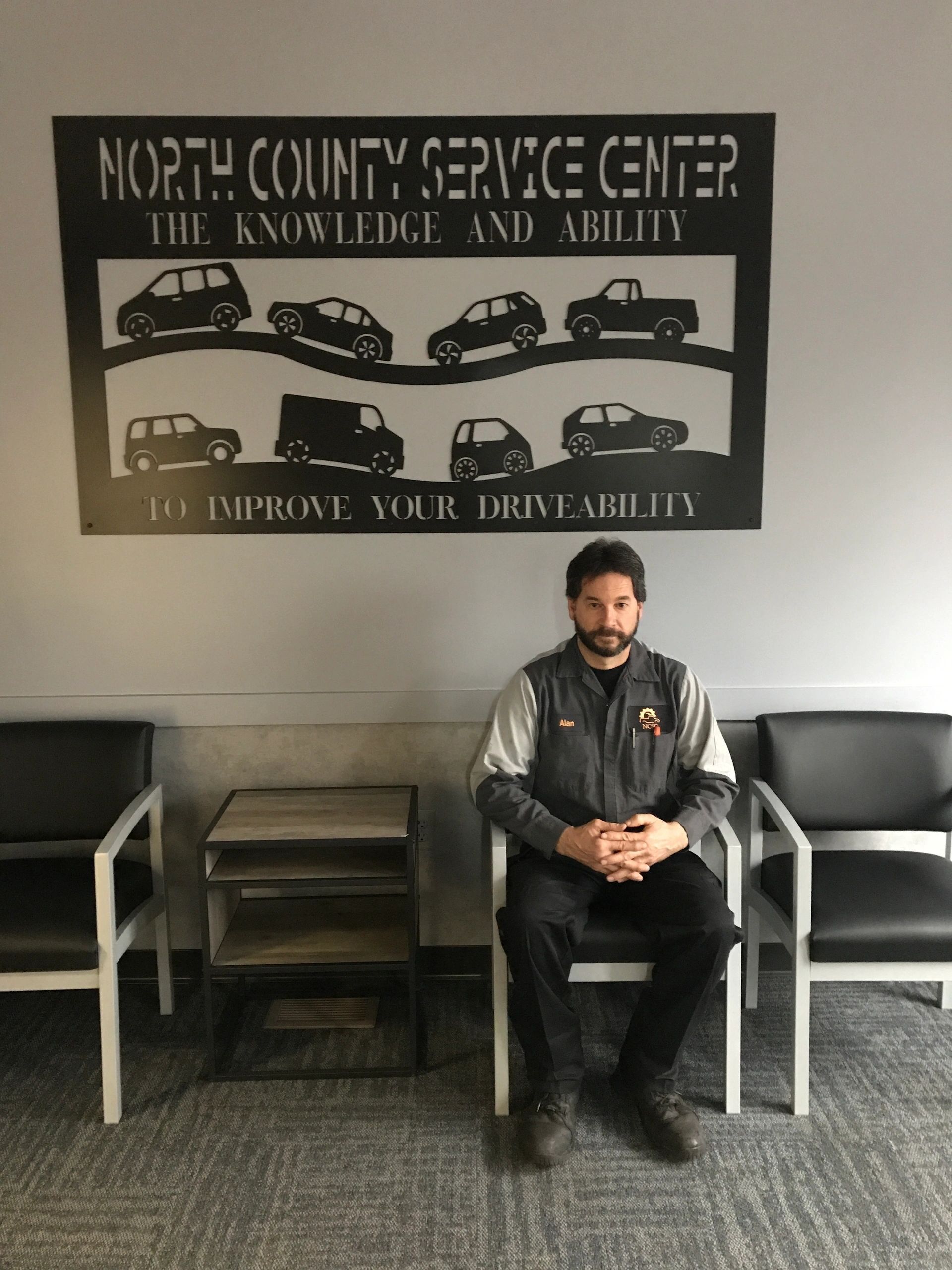 A man is sitting in a chair in front of a sign that says north county service center | North County Service Center