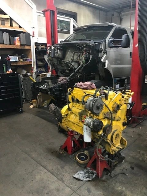 A yellow truck engine is sitting on a jack in a garage | North County Service Center