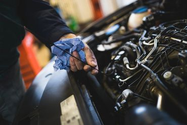 A man is checking the oil level of a car engine. | North County Service Center