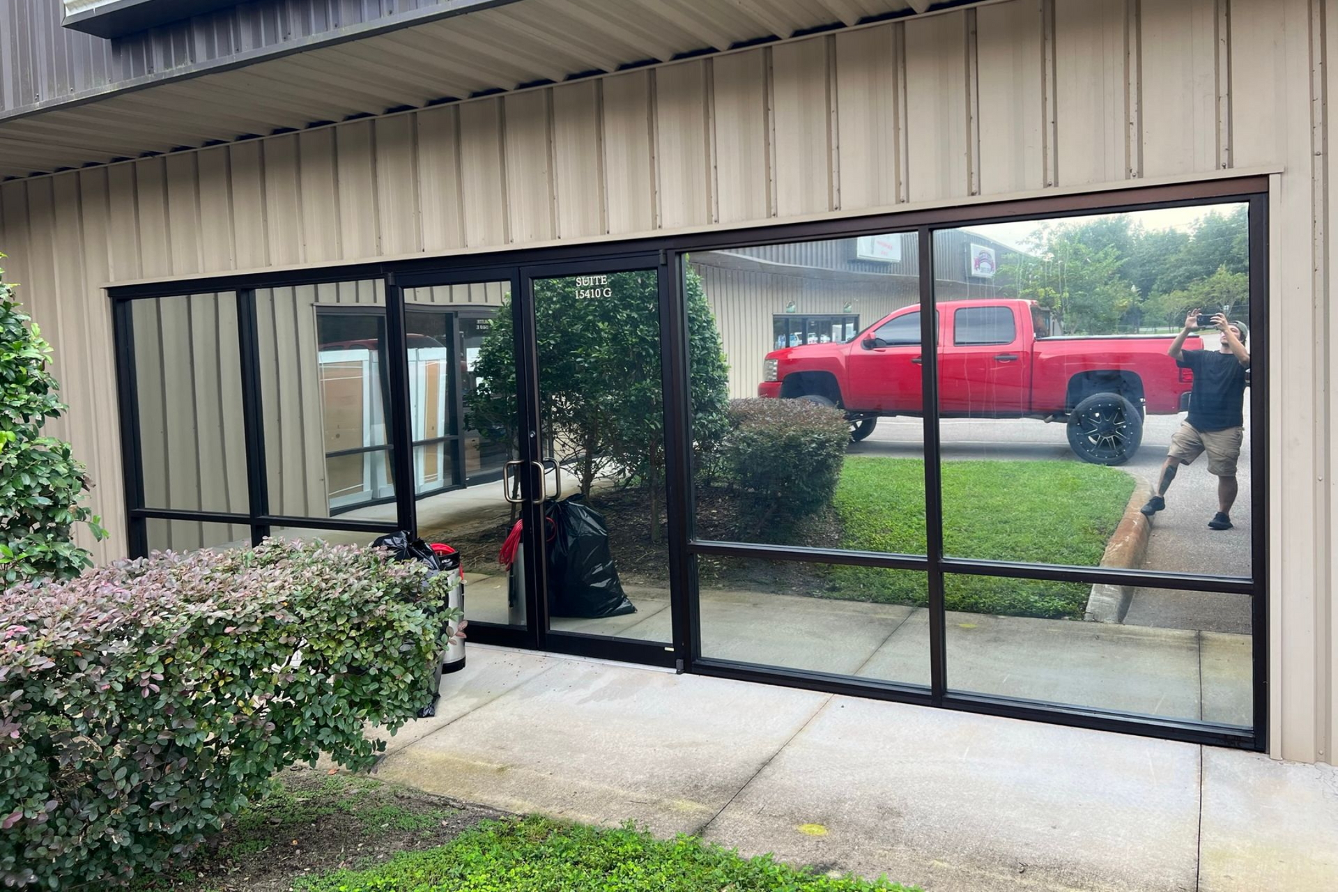 Building with large windows; a red truck and person sweeping are visible in the reflection.