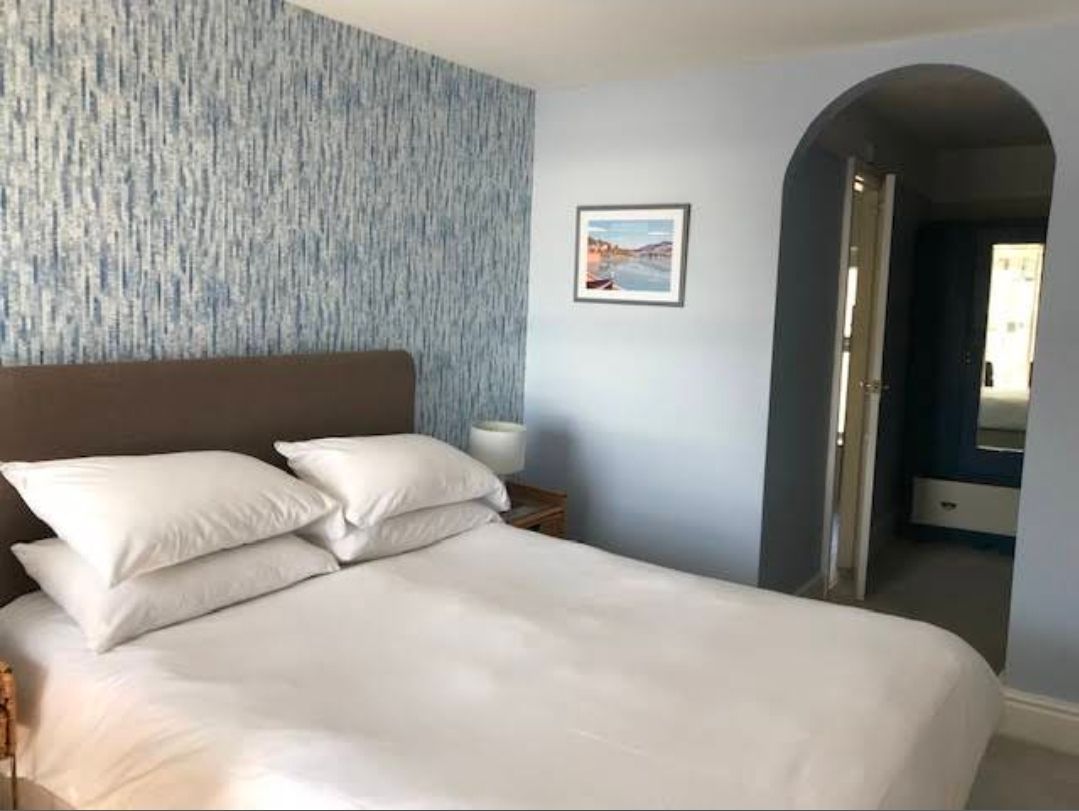 Bedroom with a large bed, white bedding, blue patterned accent wall, and an arched doorway