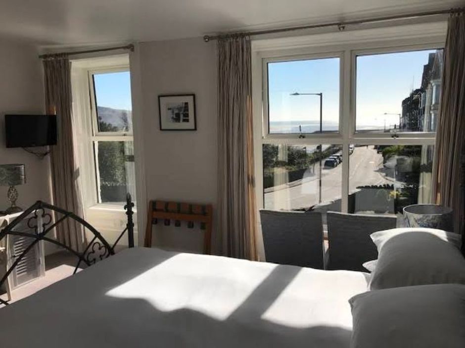 Bright bedroom with large windows, a bed, and sunlight streaming in toward a balcony and street view.