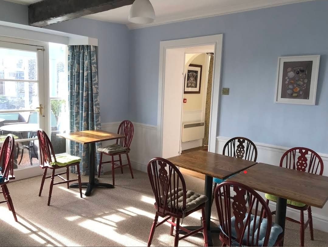 Bright dining area with tables and chairs by a sunlit window, pale blue walls, and wall art.