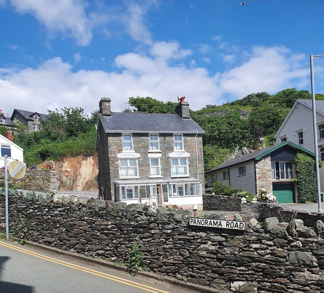 Stone cottage with white trim beside a roadside and stone wall under a blue sky