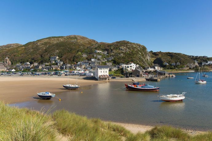 Quiet harbor with small boats on a sandy beach, white houses, and green hills under a clear blue sky