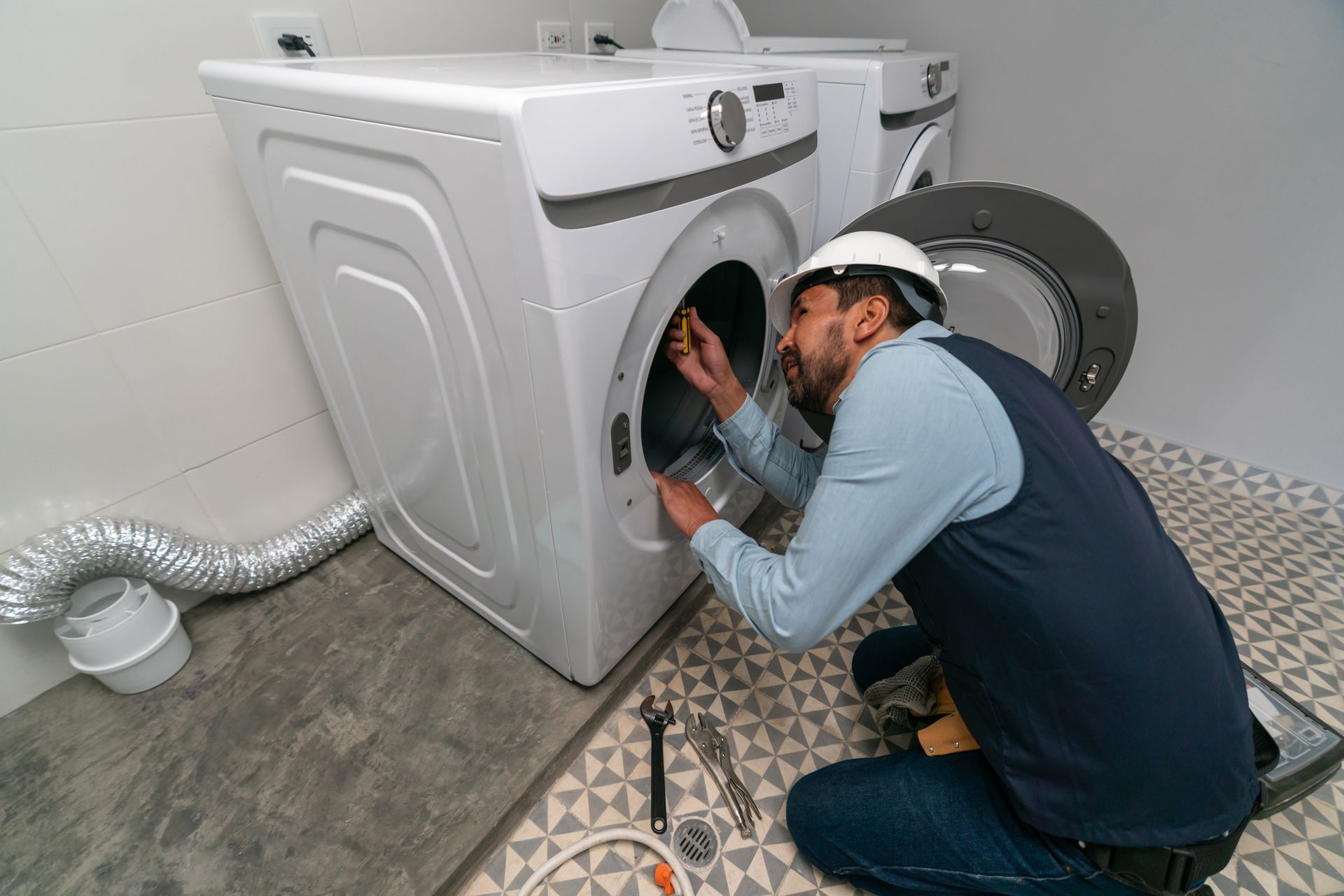 A man is fixing a washer and dryer in a laundry room.
