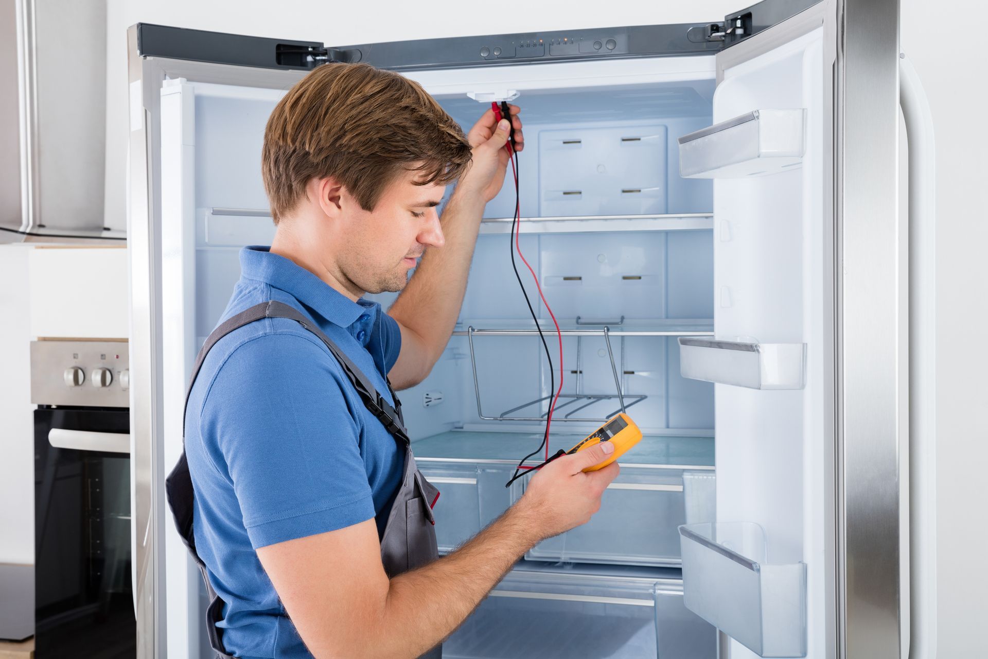 A man is laying on the floor fixing a stainless steel refrigerator.