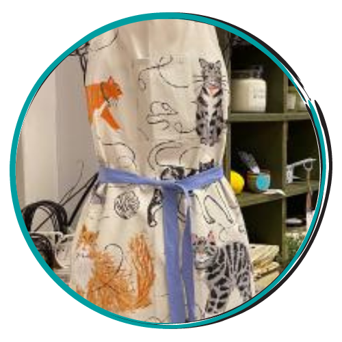 Cloth dress with animal prints tied with a blue belt, hanging beside shelves in a shop.