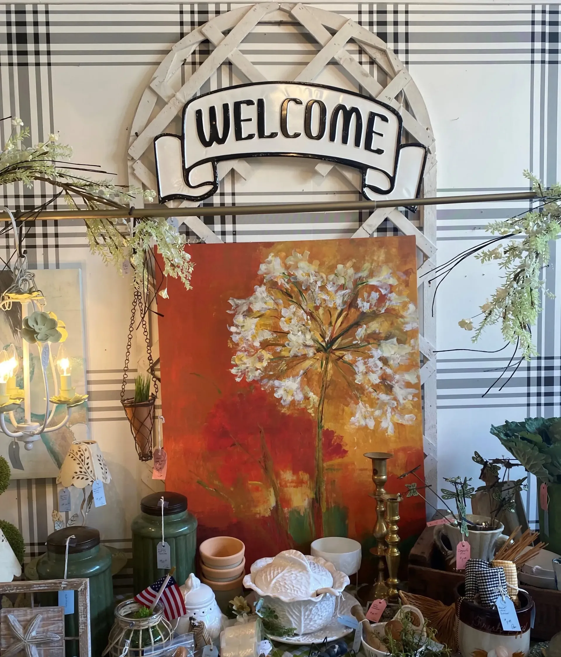 Decorated entryway with a “WELCOME” sign, autumn wall art, and plants on a plaid backdrop.