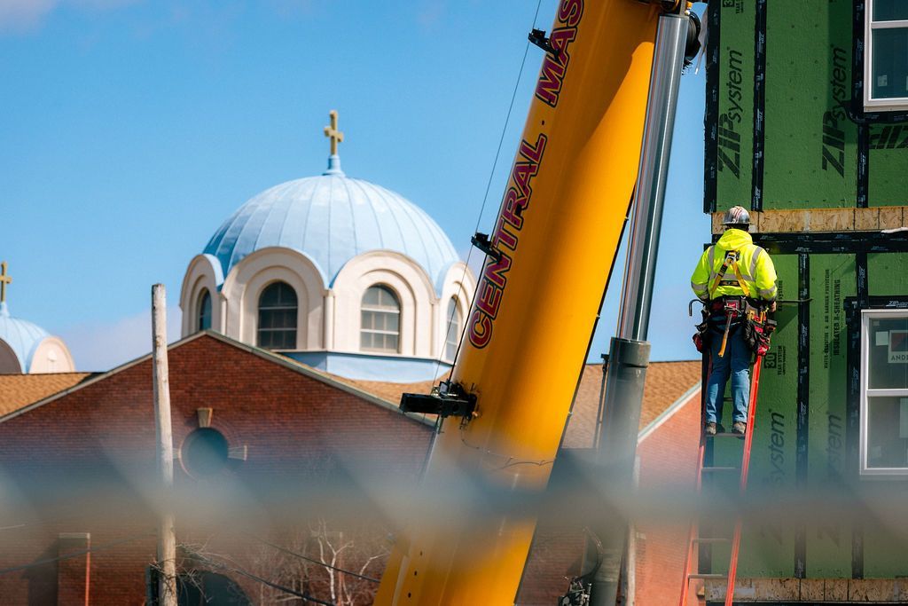Construction worker on a crane beside a domed building under a blue sky