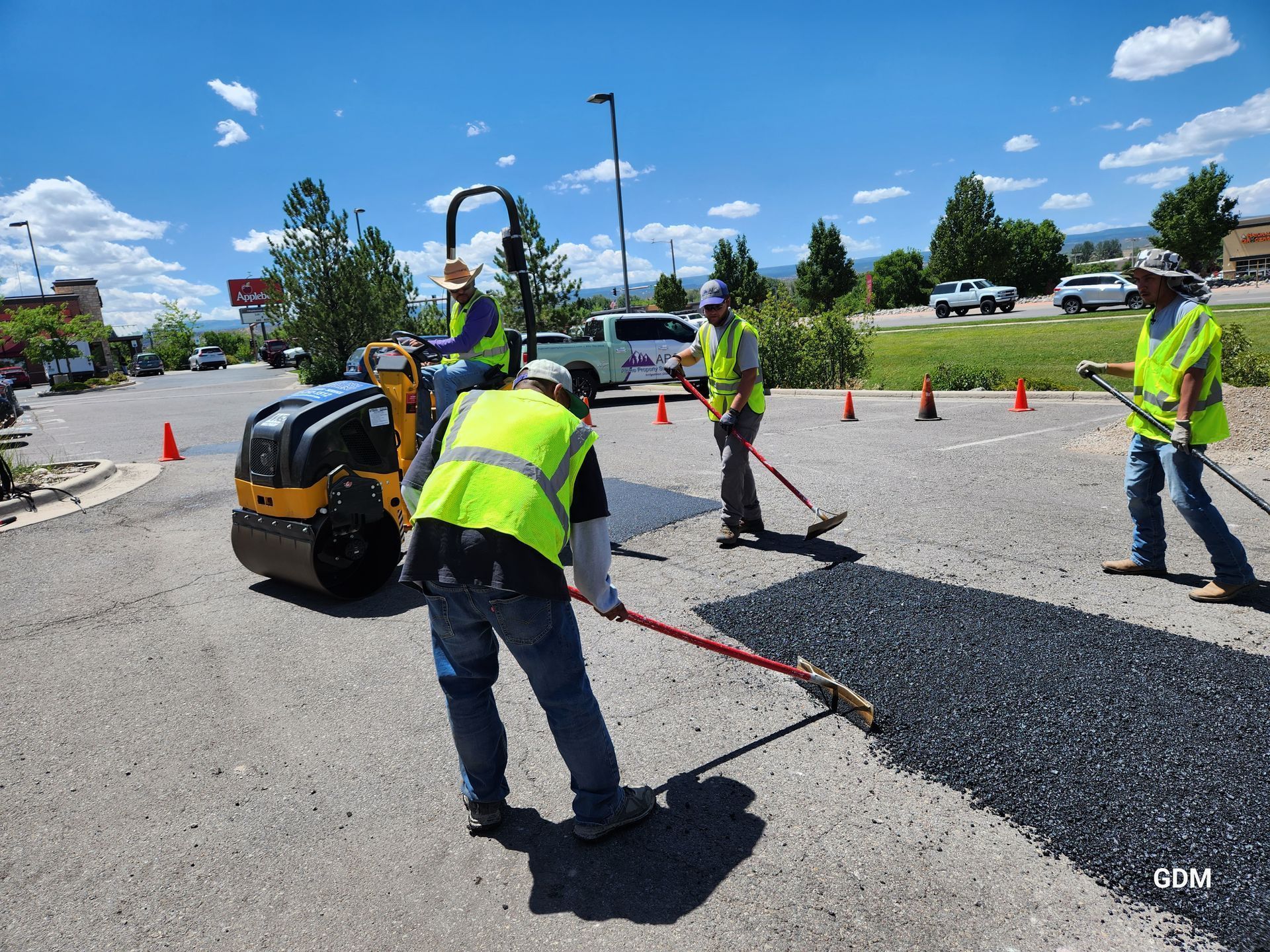 Road workers paving asphalt with a roller and rakes on a sunny day.
