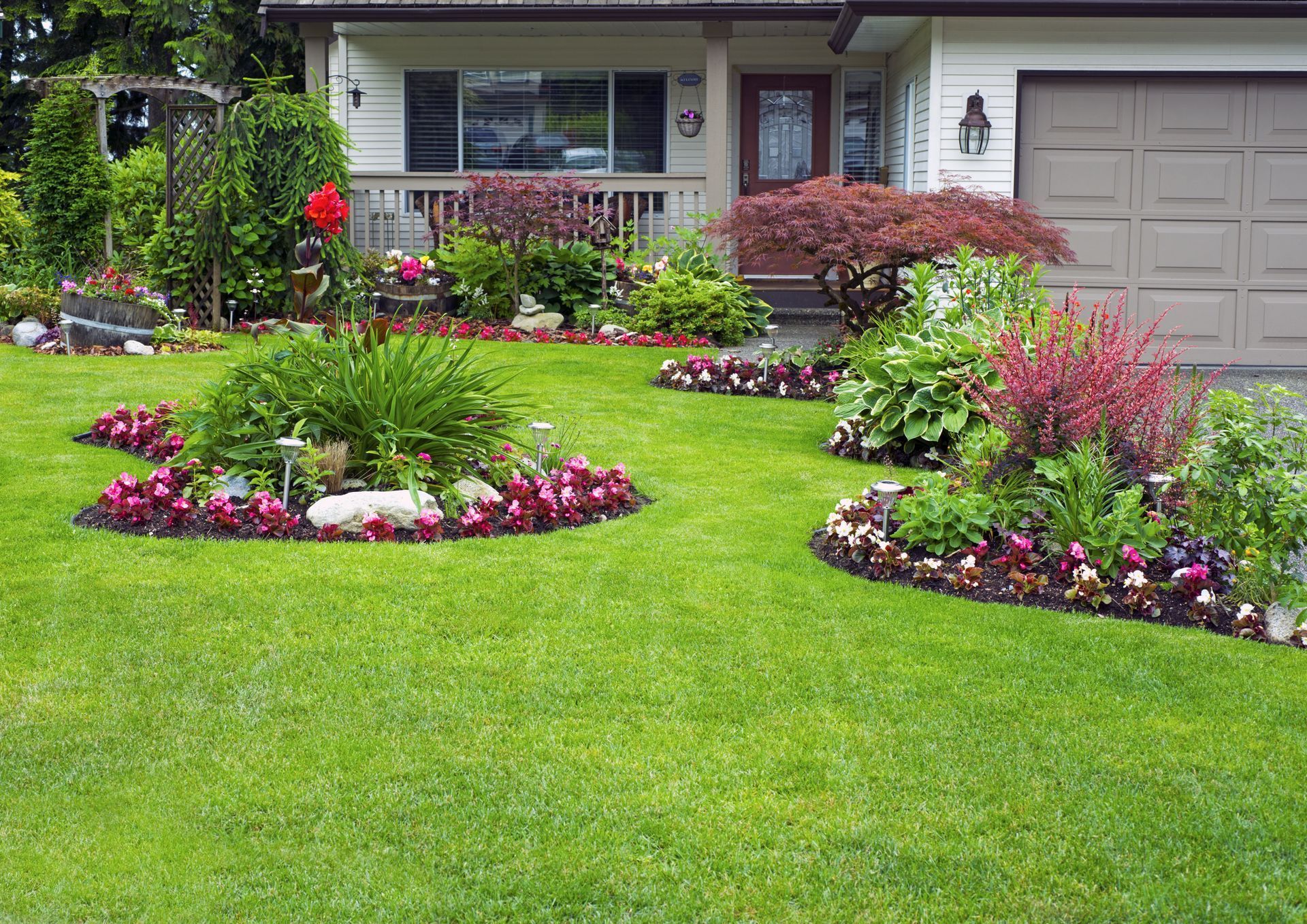 Well-manicured suburban yard with green lawn, vibrant flowerbeds, and a house with a garage.
