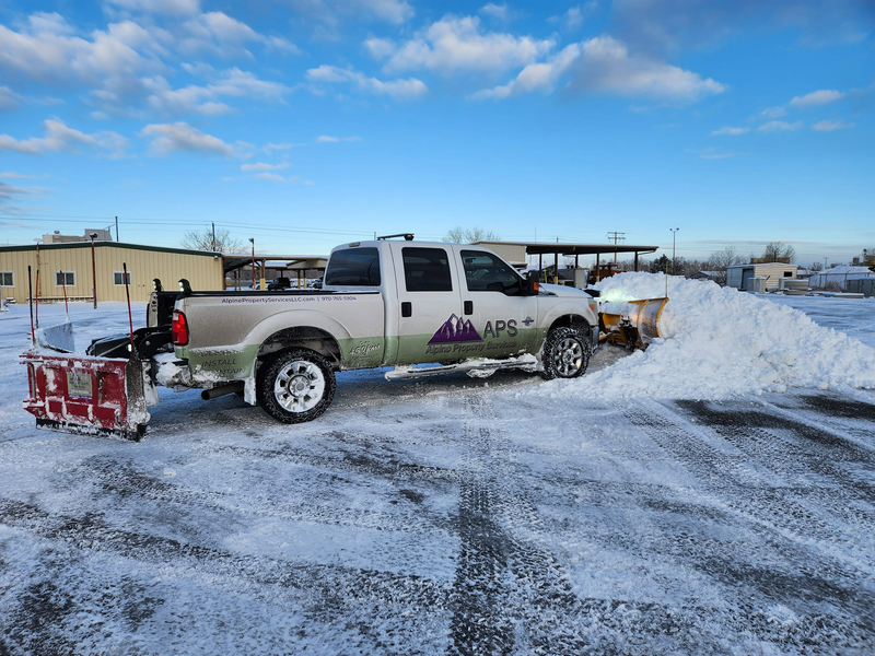 Snowplow truck clearing snow from a parking lot on a cloudy day.