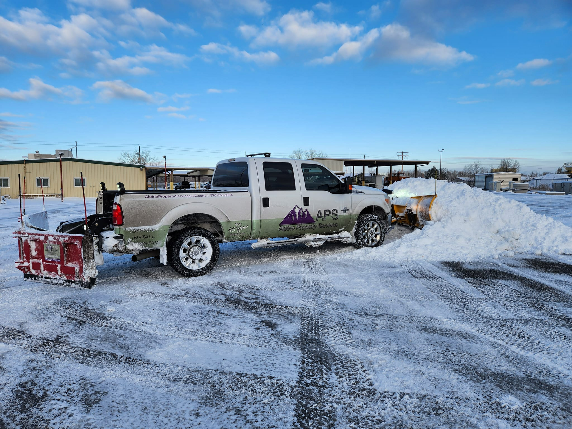 Snowplow truck clearing snow, outdoor in winter. White truck, snow, and a blue sky.