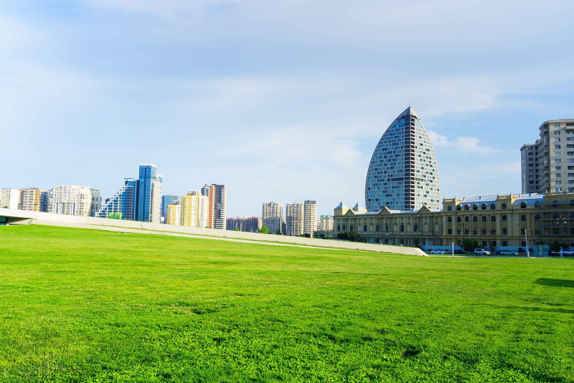 Wide green lawn with a modern city skyline and blue sky in the background