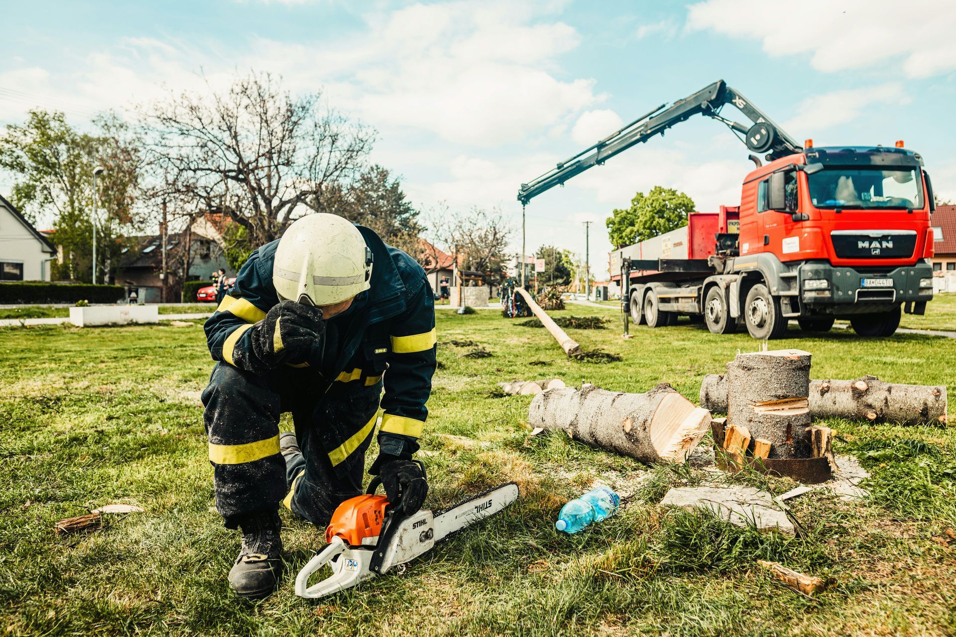 Firefighter using a chainsaw near fallen tree limbs beside a red truck with an extended crane arm