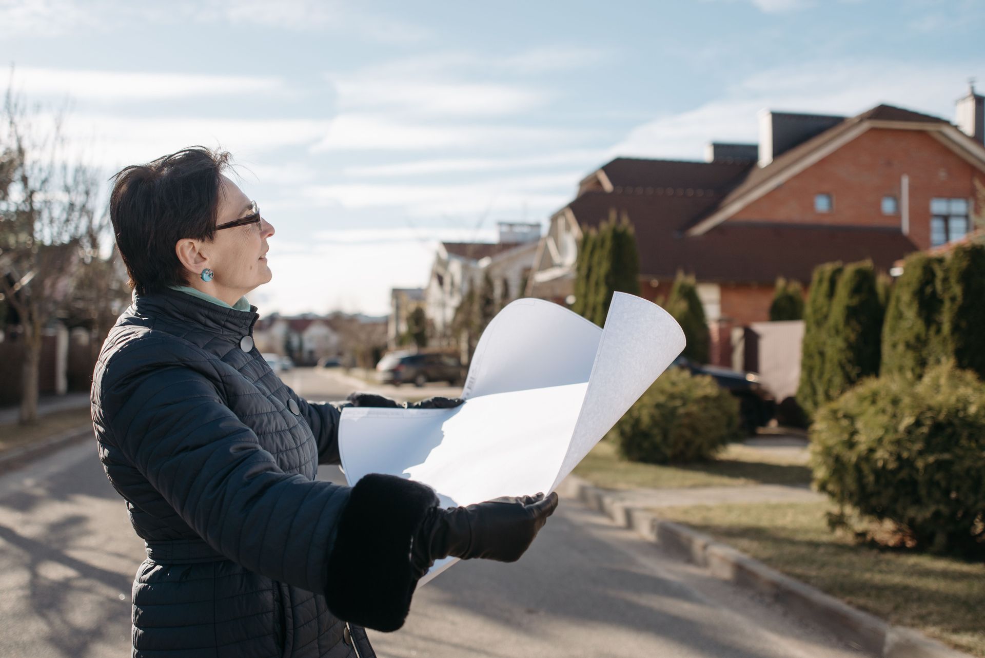 Person holding unfolded papers outdoors in a suburban neighborhood, looking up at homes.
